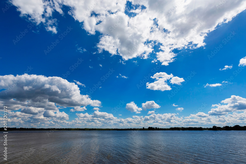 Panoramic landscape of summer day at a river with blue cloudy sky.
