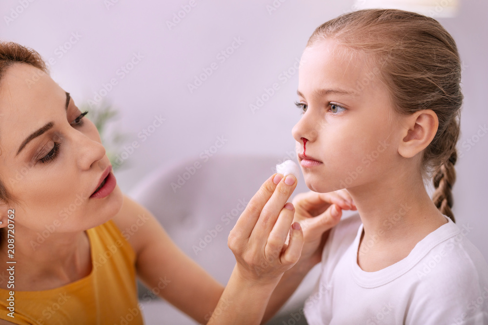 Caring mother. Nice young woman looking at her daughter face while wiping away her blood Caring mother. Nice young woman looking at her daughter face while wiping away her blood