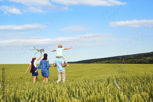 A happy family is walking in a wheat field in the summer. Back view.