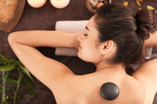 Young woman undergoing hot stone therapy on massage table at spa salon, top view
