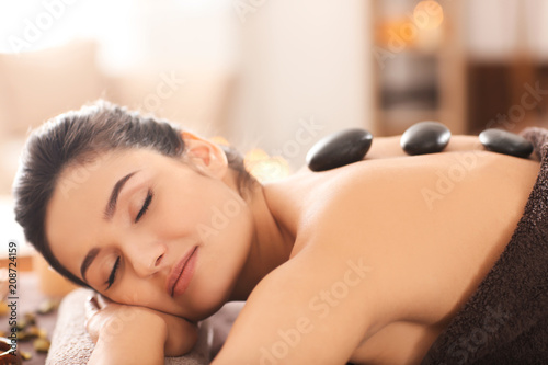 Young woman undergoing hot stone therapy on massage table at spa salon