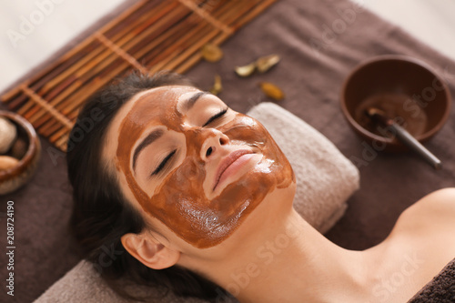 Young woman with face mask relaxing on massage table at spa salon