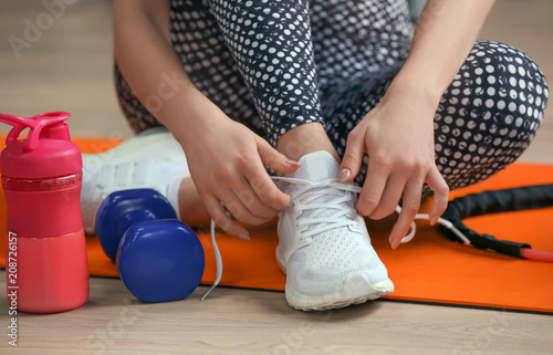 Young woman tying shoelaces on floor in gym, closeup