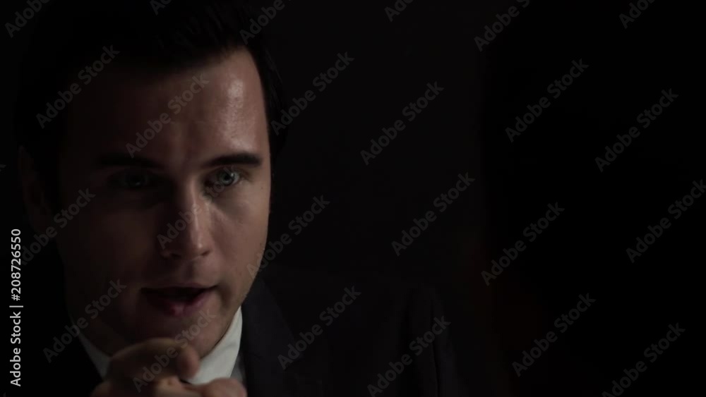 Upset man in formal business suit talking and  asking questions in dark  investigation room