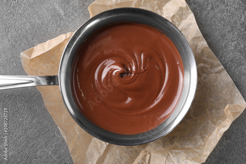 Bowl with tasty melted chocolate on grey table, top view
