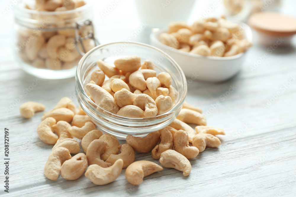 Glass bowl with tasty cashew nuts on light wooden background Glass bowl with tasty cashew nuts on light wooden background