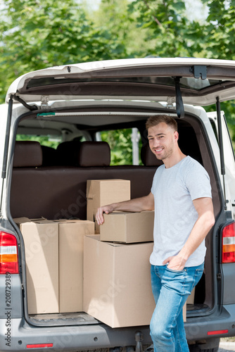 happy young man standing near car trunk with boxes for relocation into new house