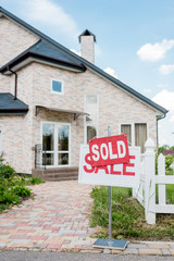 sold sign on wooden placard with sale sign in front of modern cottage