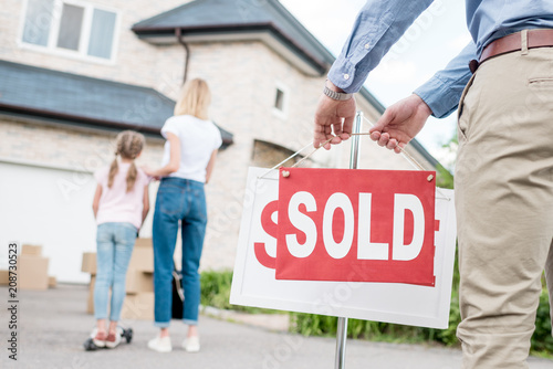 partial view of realtor hanging sold sign in front of people moving into new house photo