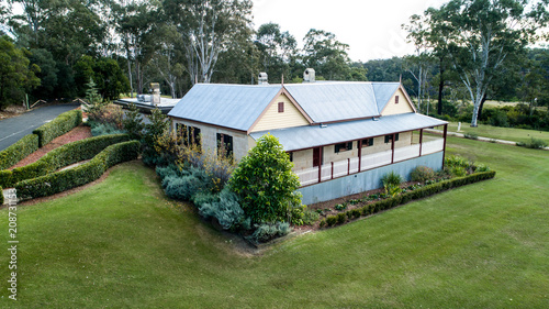 Aerial view of colonial sandstone cottage house with picket fence, garden, grass and eucalyptus gum trees
