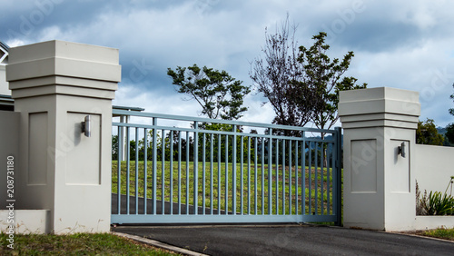 Metal driveway private residence property entrance gates set in brick fence with garden trees in background