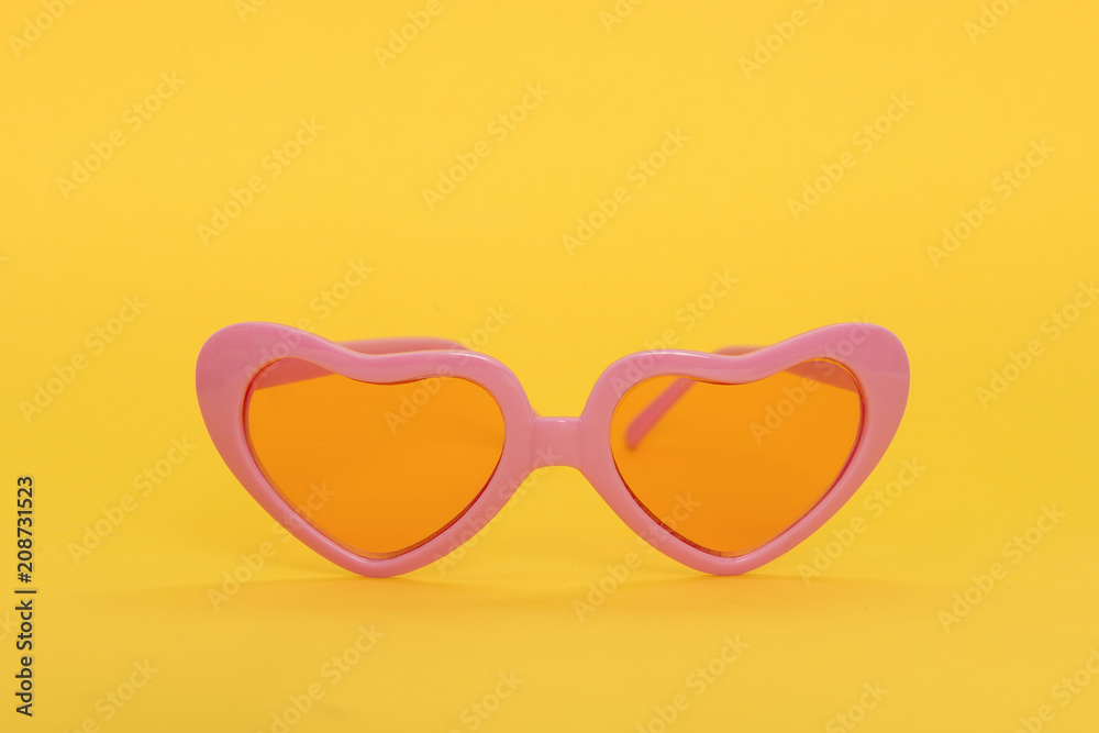 Pink heart shaped sunglasses on a yellow background Pink heart shaped sunglasses on a yellow background