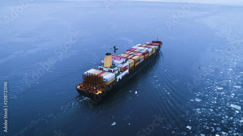 Aerial Shot of the Cargo Ship Moving Through the Sea. In the Background Winter Landscape.