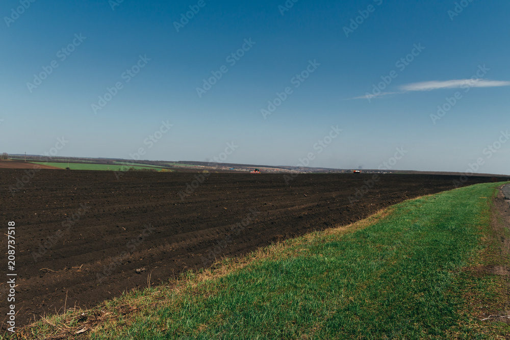 Summer day two tractors to plow, plow the soil on sloping, cornfield. Agricultural land treatment before planting.