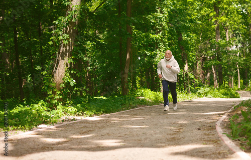 Elderly man running in green forest, copy space