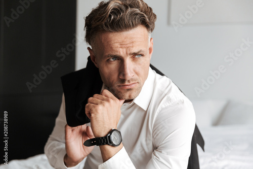 Concentrated man dressed in suit sitting on bed