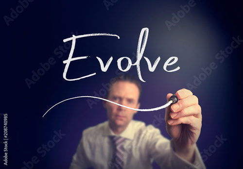 A businessman writing a Evolve concept with a white pen on a clear screen.
