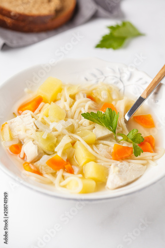 Chicken soup with noodles and vegetables in a white plate.