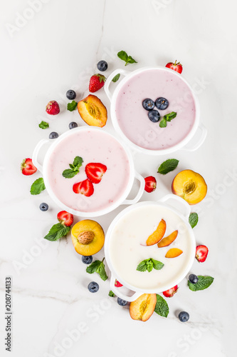 Summer healthy diet dinner, vegan food, dessert, various sweet creamy fruit & berry soups - strawberry, peach, blueberry, white marble background top view copy space