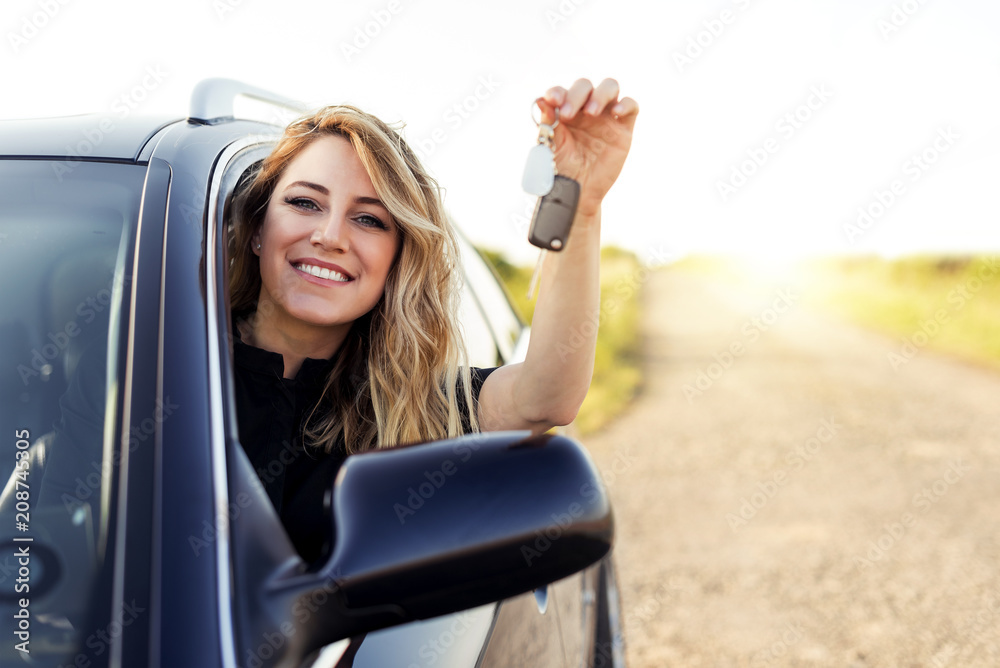 An attractive woman in a car holds a car key in her hand.
