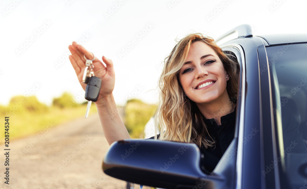 An attractive woman in a car holds a car key in her hand.