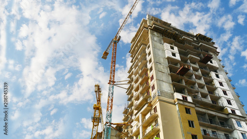 Two cranes near construction building against blue sky. Construction site.