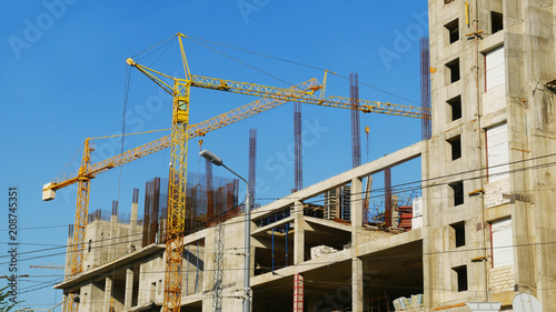 Two cranes near construction building against blue sky. Construction site.