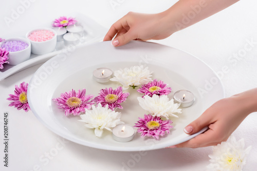cropped shot of woman holding bath for nails with flowers and aroma candles at table in beauty salon