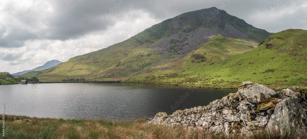 A dry stone wall leads to the fishing lake of Llyn y Dywarchen in the  Snowdonia National Park. The beautiful mountain y Garn is in the distance.  Stock Photo | Adobe Stock