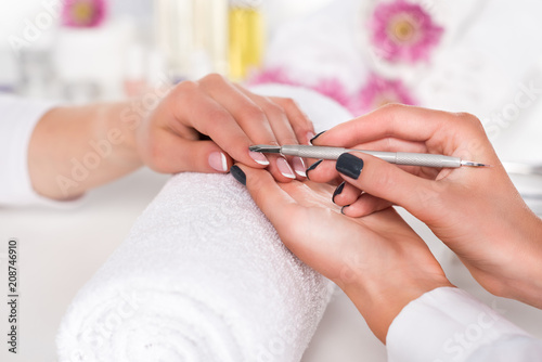 close up image of  woman receiving manicure by beautician with cuticle pusher at table with flowers and towels in beauty salon