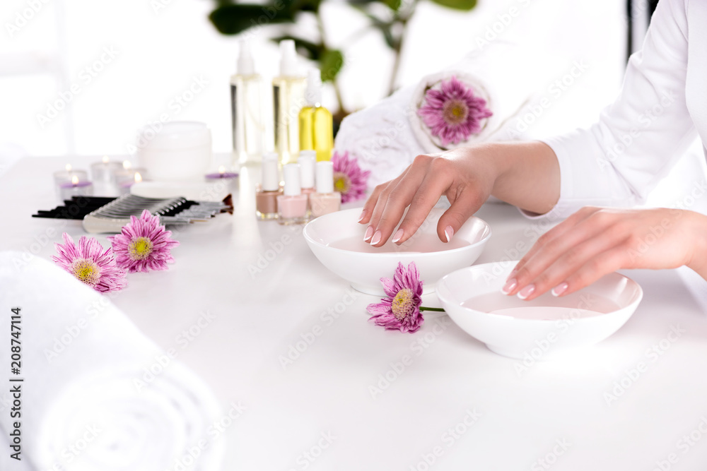 cropped image of woman receiving bath for nails at table with flowers, towels, candles, aroma oil bottles, nail polishes, cream container and tools for manicure in beauty salon cropped image of woman receiving bath for nails at table with flowers, towels, candles, aroma oil bottles, nail polishes, cream container and tools for manicure in beauty salon