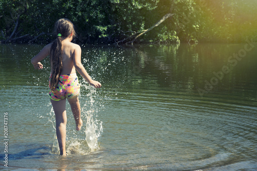 Fototapeta Naklejka Na Ścianę i Meble -  A little girl splashing her foot in the water. Children and summer holidays.