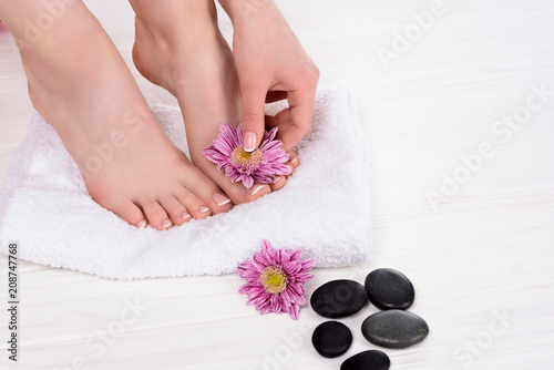 partial view of barefoot woman on spa treatment with towel, flowers and spa stones