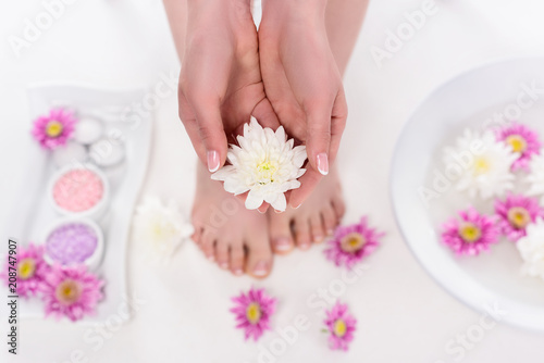 partial view of barefoot woman holding flower on procedure in beauty salon