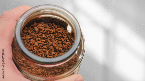 Instant coffee background. Hand holding a pot of granulated instant coffee and blank space on side of text.