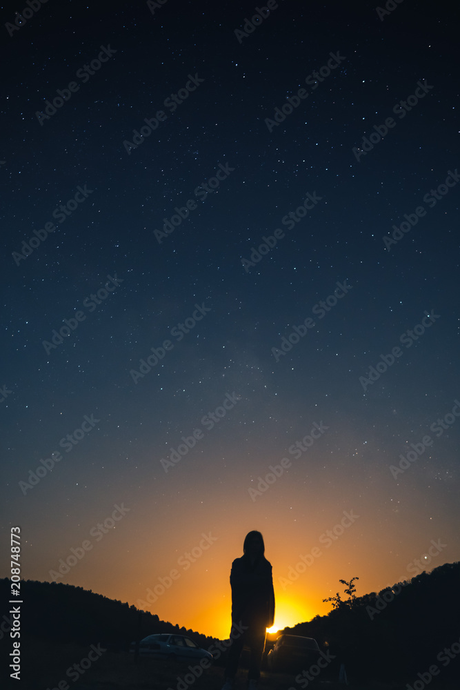 alone woman silhouette in mountains, girl wrapped up in a plaid looks at the sky, enjoying view of amazing night sky full of stars, vertical photo