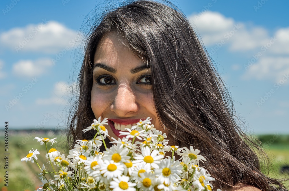 Young charming brunette girl with a bouquet of white field chamomiles on a summer sunny day Young charming brunette girl with a bouquet of white field chamomiles on a summer sunny day