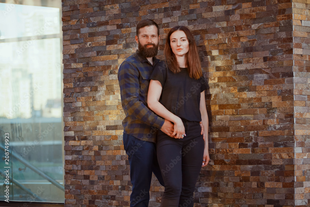 Stylish young couple is spending time together outdoors. Attractive woman and handsome bearded man are posing on brick background. Stylish young couple is spending time together outdoors. Attractive woman and handsome bearded man are posing on brick background.