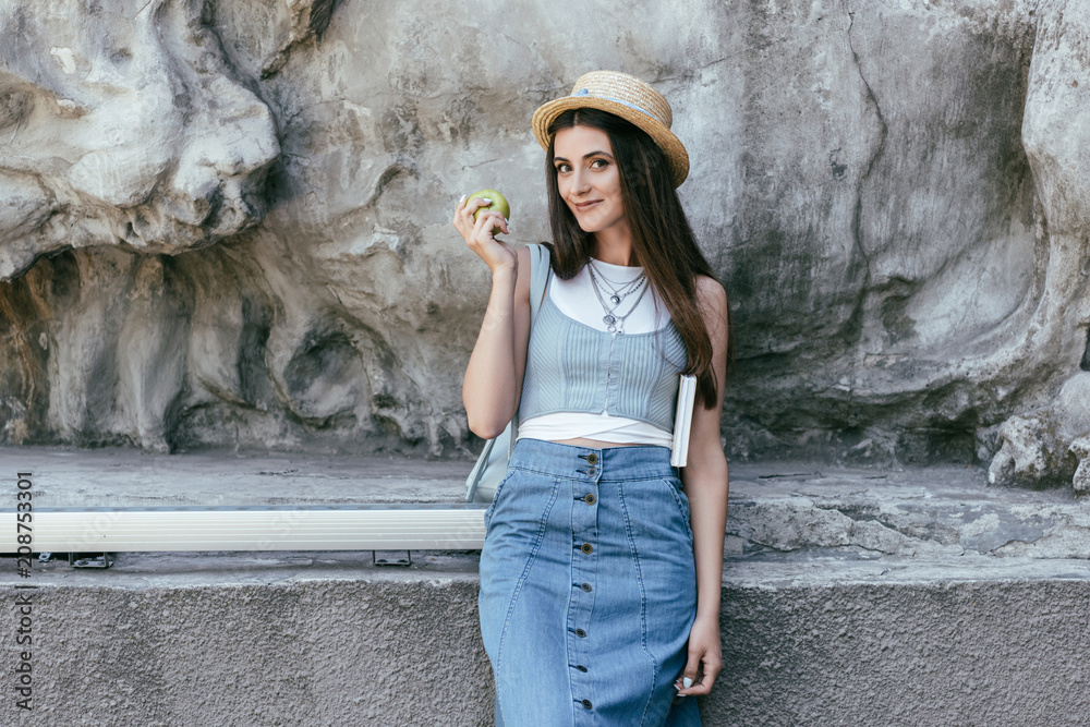 beautiful smiling young woman in hat holding apple and book