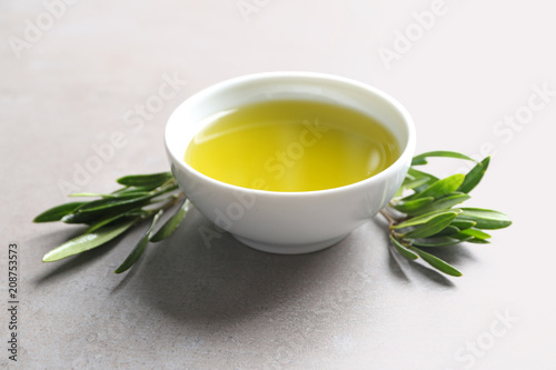 Bowl with olive oil and green leaves on grey background