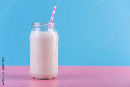 Glass bottle of fresh milk with straw on pastel background. Colorful minimalism. Healthy dairy products with calcium