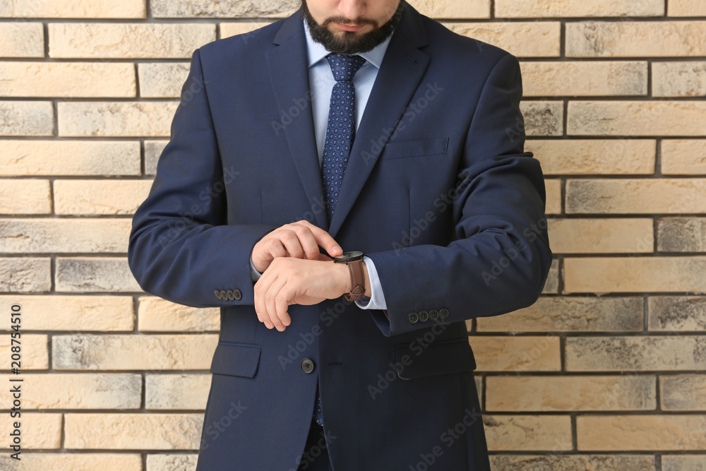 Man looking at his watch on brick background. Time management concept Man looking at his watch on brick background. Time management concept