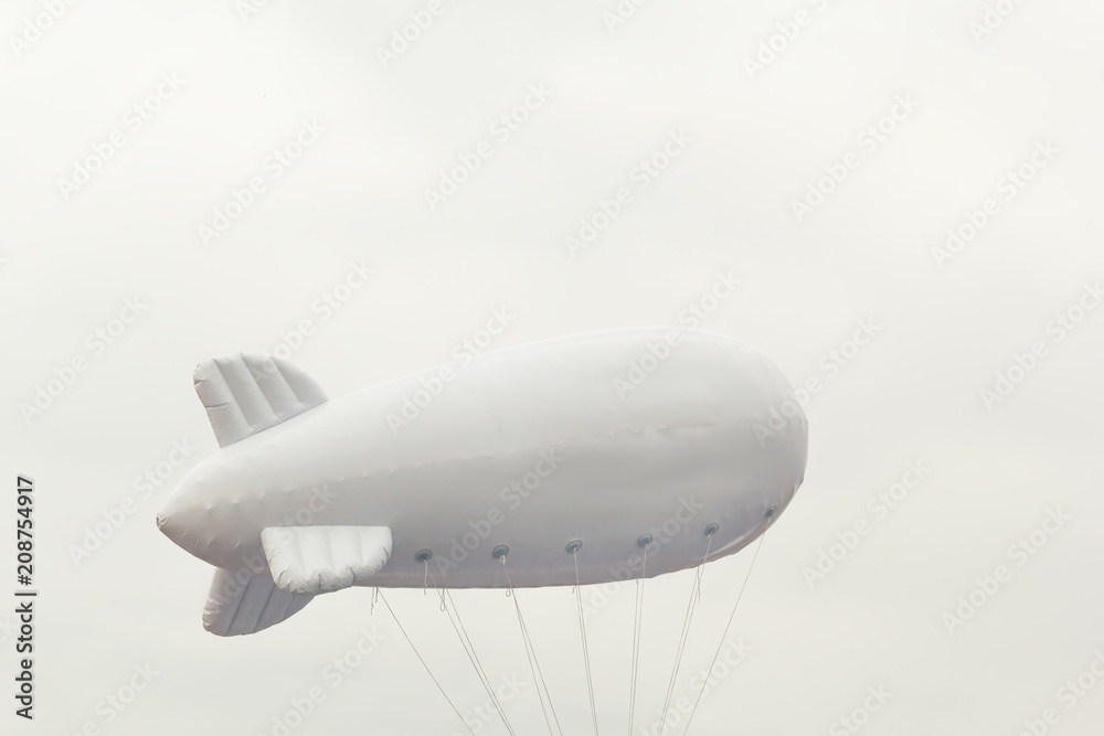 Fototapeta premium White inflatable dirigible with a place for a logo on a background of a gray sky with clouds. Copy space