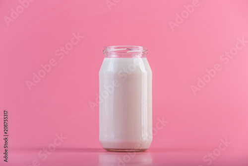 Glass bottle with fresh milk on pink background. Colorful minimalism. Healthy dairy products with calcium