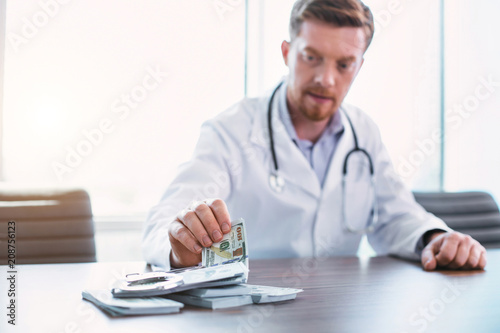 My money. Handsome bearded doctor sitting at the table and taking bribes