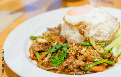 delicious Thai food garlic and pepper with pork and Fried egg with jasmin rice closeup with carrot cucumber Spring onion and coriander leaves on top in white plate .delicious Thai food