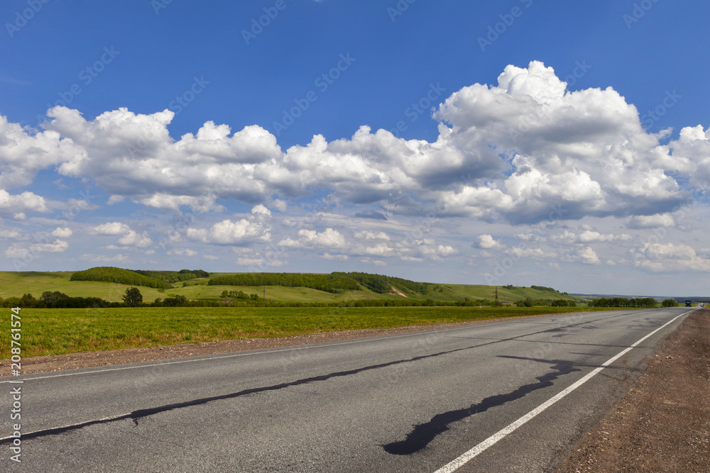 Road in the field, long distance trail in the field. Beautiful green hills. Blue sky with fluffy clouds Road in the field, long distance trail in the field. Beautiful green hills. Blue sky with fluffy clouds