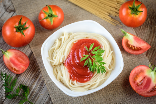 Spaghetti pasta with tomato sauce in plate and tomatoes on wooden table.
