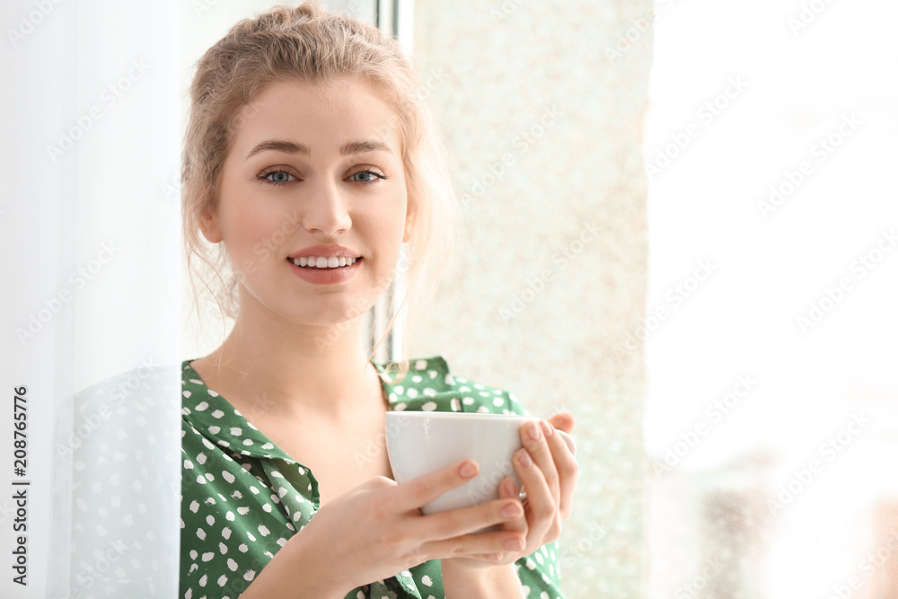 Young woman drinking tea near window indoors Young woman drinking tea near window indoors