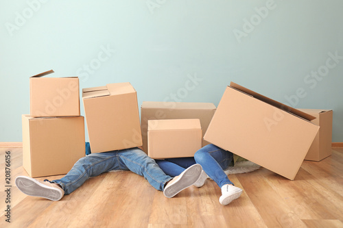 Young couple buried under heap of boxes indoors. Moving into new house